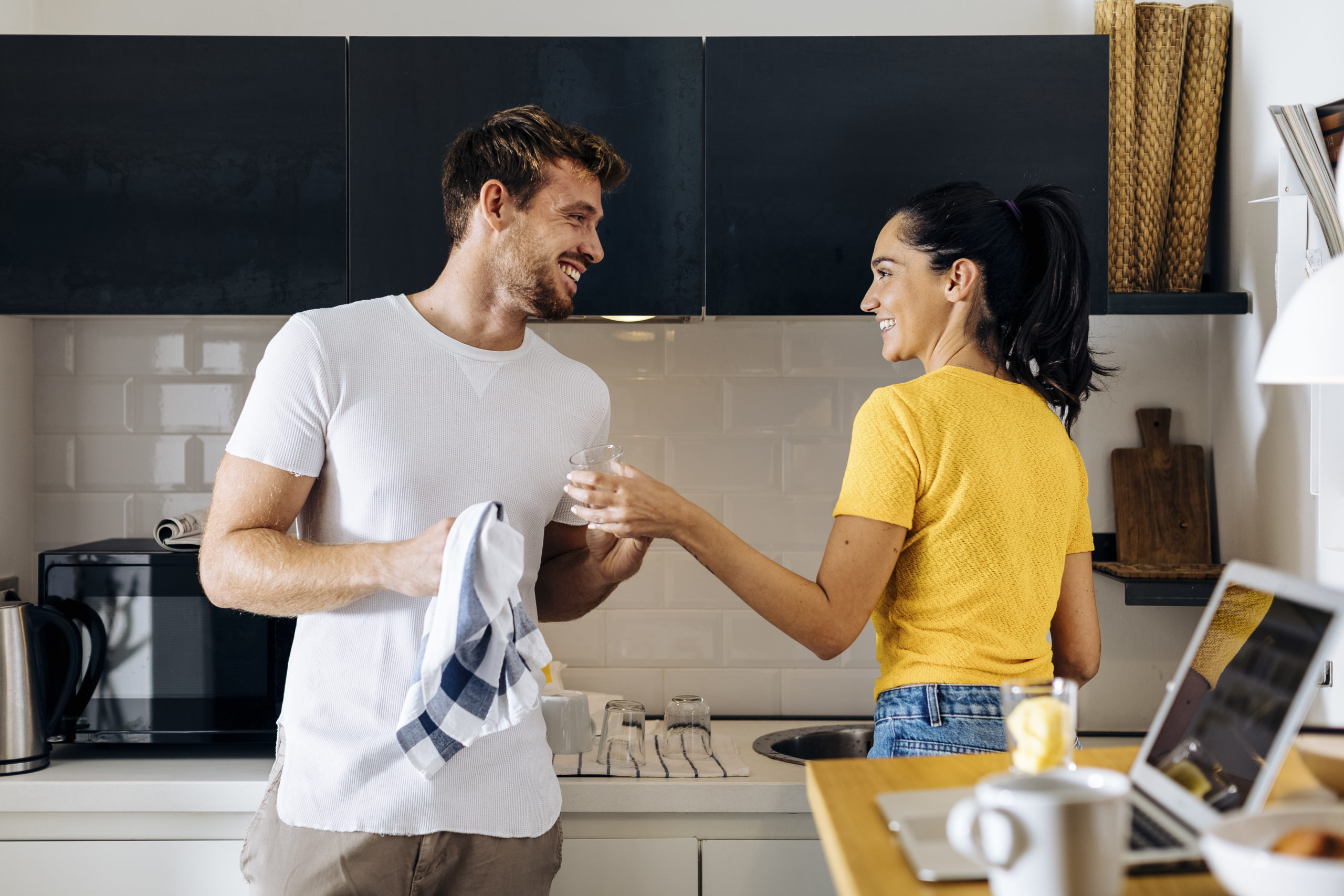 Happy young couple smiling at each while washing dishes and navigating a love-hate relationship.