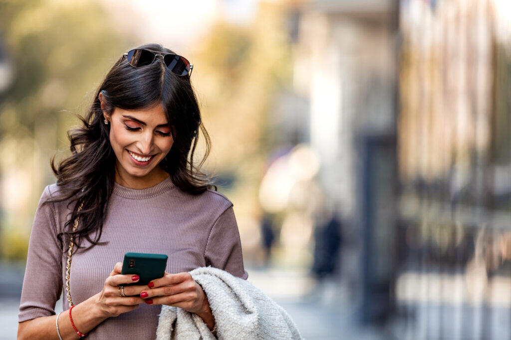 Middle-aged woman walking along the street and smiling while using mobile phone for online dating in Buffalo NY.